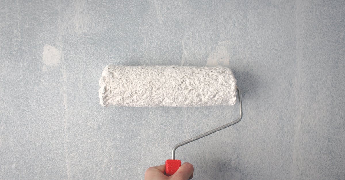 A person's hand using a paint roller to apply white paint on a wall.